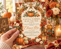A hand holding a card with a pumpkin and fall-themed design, surrounded by a table with decorations and flowers.