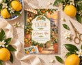 a baby shower invitation with a scenic background of a garden and a sunset. The invitation is surrounded by various objects, including lemons, flowers, and a pair of scissors.