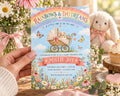 A hand holding a colorful baby shower invitation with a baby carriage and flowers, with a stuffed bunny rabbit in the background.