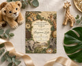 a baby shower invitation with a jungle theme, surrounded by stuffed animals, a leaf, and a giraffe figurine.