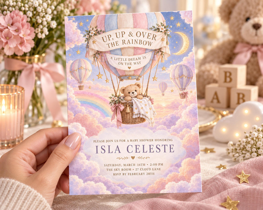 A hand holding a baby shower invitation featuring a teddy bear in a basket on a hot air balloon, surrounded by clouds and stars.