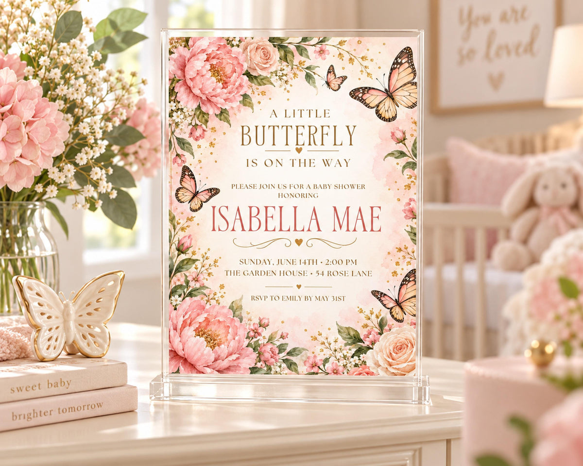 A baby shower invitation featuring a pink and white floral design with butterflies, placed on a table with books and a vase of flowers.