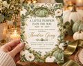 A hand holding a baby shower invitation with a pumpkin and floral design.