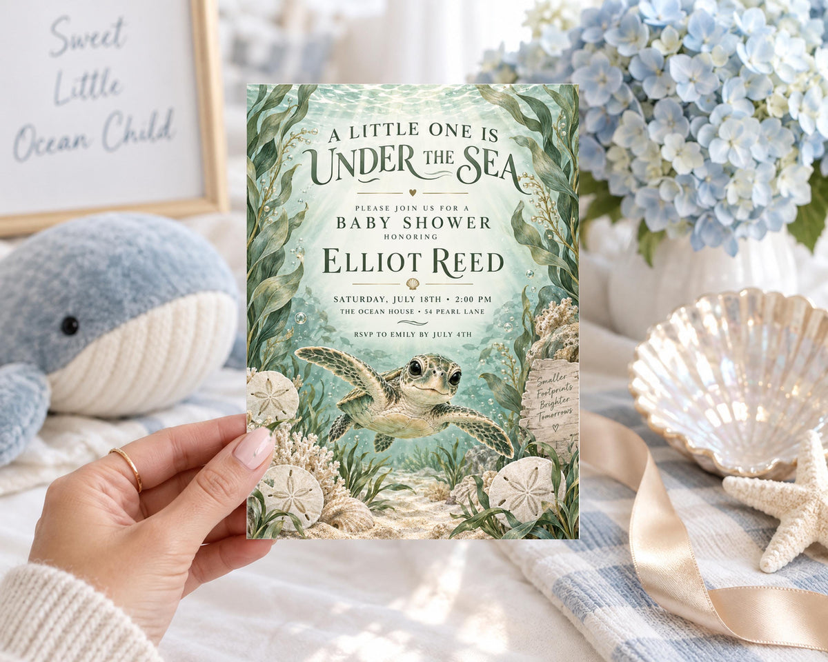 A person is holding a baby shower invitation for a baby named Elliot Reed, featuring an underwater scene with a turtle and seashells.