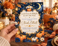 A hand holding a baby shower invitation with a pumpkin and autumn theme.