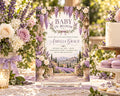 The image is a baby shower invitation featuring a beautiful floral design with purple and white flowers, surrounded by a table with a cake, flowers, and other decorations.